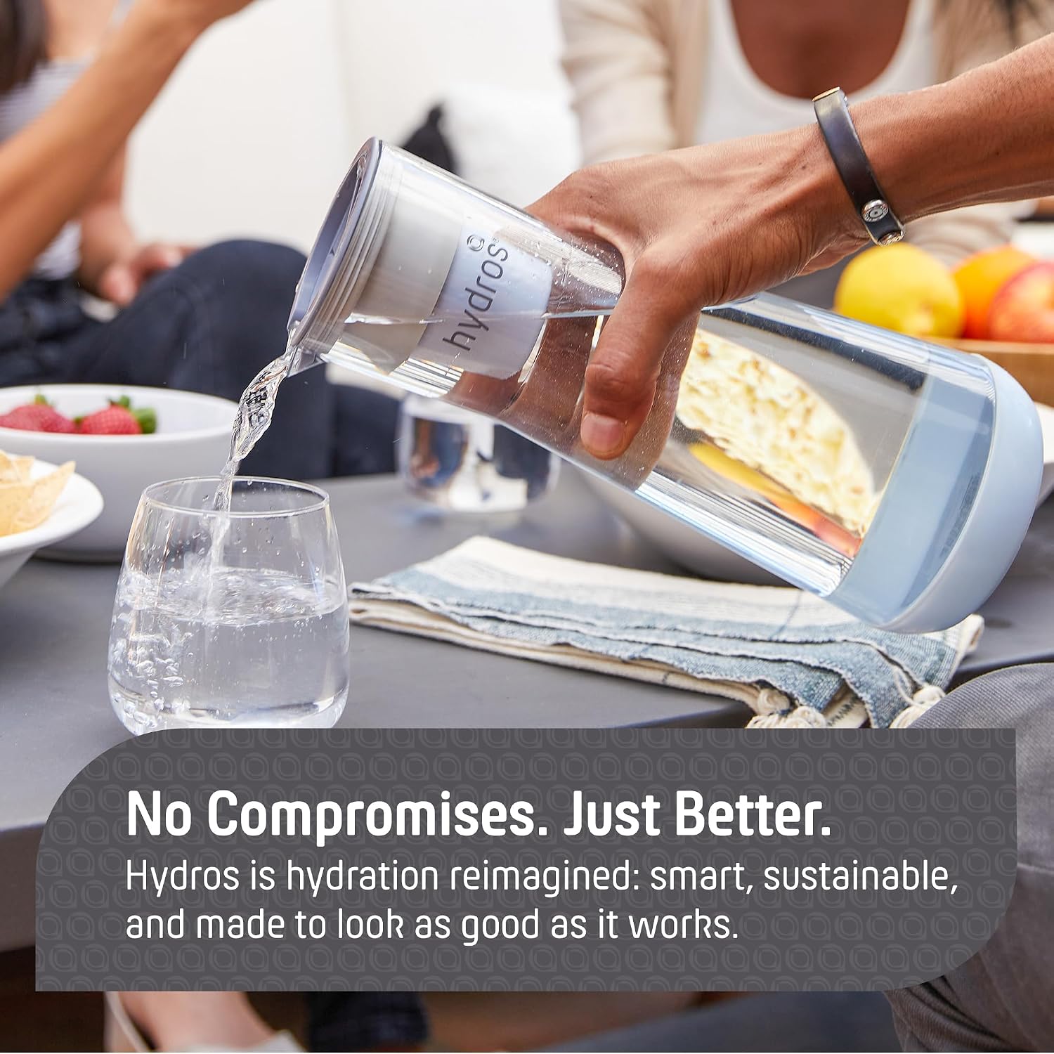 A person pouring water from a clear Hydros insulated water bottle into a glass at a dining table, with a promotional text banner overlaid at the bottom.